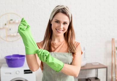 Junge Hausfrau zieht voller Vorfreude Gummihandschuhe an, bevor sie die Wohnung putzt.