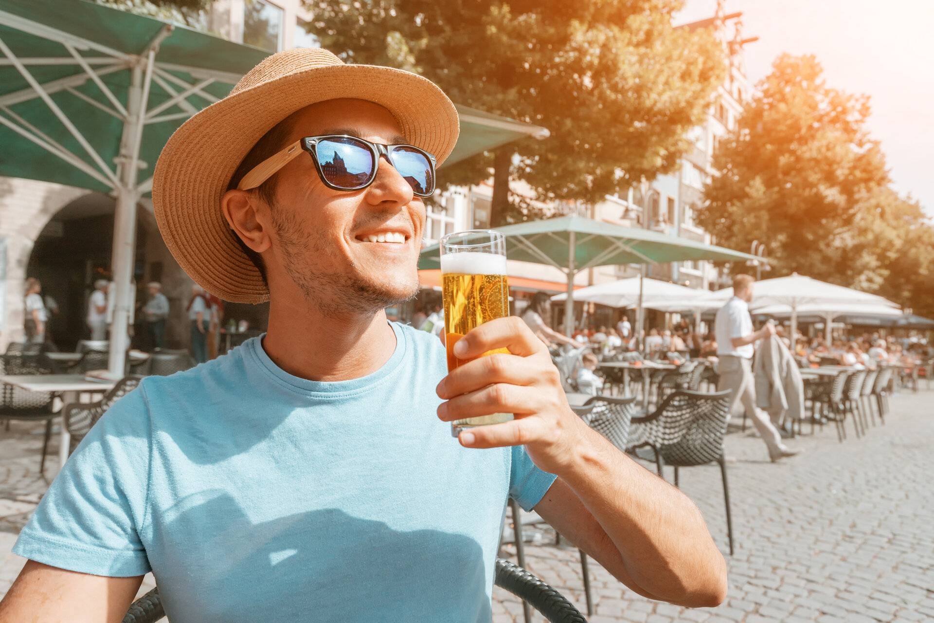 Glücklicher Mann mit Sonnenbrille und Hut, der traditionelles Kölner Kölsch-Bier im Pub im Freien probiert und trinkt