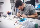 In einer Elektronikwerkstatt repariert ein Mechaniker ein Smartphone, verwendet eine Pinzette als eines der vielen Arbeitsgeräte.