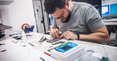 In einer Elektronikwerkstatt repariert ein Mechaniker ein Smartphone, verwendet eine Pinzette als eines der vielen Arbeitsgeräte.