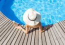 Frau mit großem Sonnenhut und Cocktailgetränk entspannt am runden Swimmingpool, mit blauem Wasser im Freien