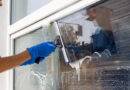 Ein Angestellter eines professionellen Reinigungsdienstes in einem Overall wäscht das Glas der Fenster an der Fassade des Gebäudes.