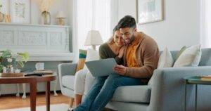 Laptop, Wohnzimmer und Paar suchen Website-Informationen für Hausinvestitionen, Darlehen oder Immobilien Diskussion auf Sofa. Junge Leute auf Couch mit PC Internet, Planung der Zukunft zusammen