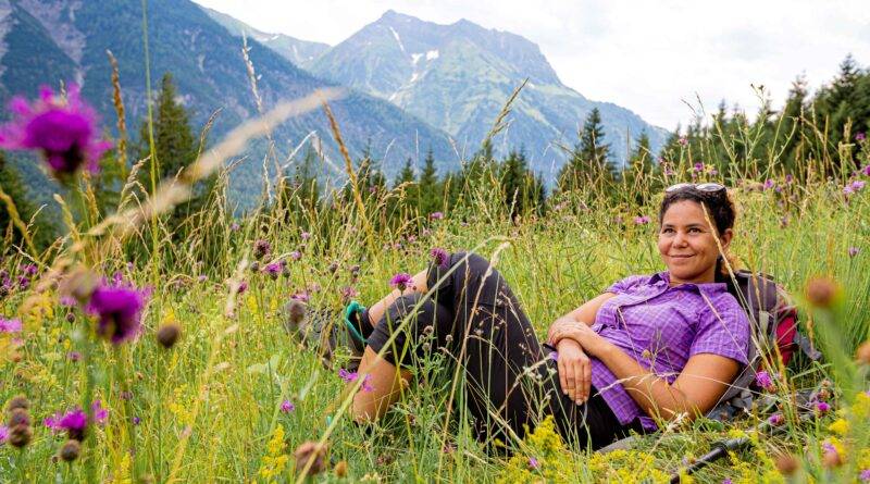 Frau in lila Hemd entspannt auf einer Blumenwiese in den Allgäuer Alpen – ideale Umgebung für eine freie Taufe im Allgäu