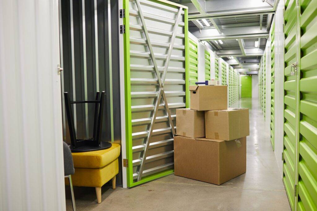 Offene Self-Storage-Einheit mit gestapelten Kartons und einem gelben Hocker