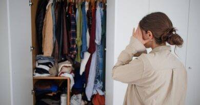 Frau steht ratlos vor überfülltem Kleiderschrank