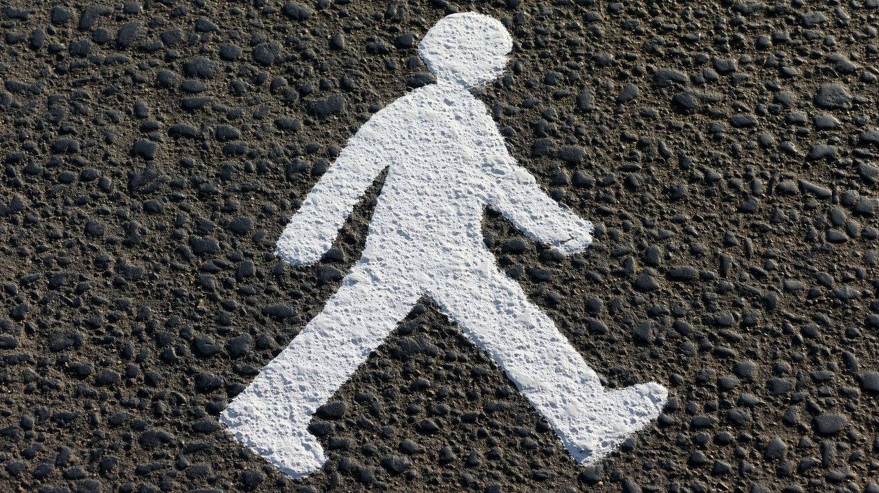 Weisse Strassenmarkierung in Form einer gehenden Person auf schwarzem Asphalt zur Orientierung von Fussgaengern