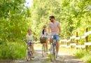 Familie, Freizeit und Menschenkonzept - glückliche Mutter, Vater und kleine Tochter fahren im Sommerpark Rad.
