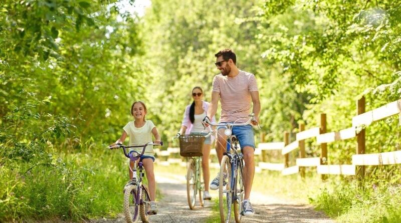 Familie, Freizeit und Menschenkonzept - glückliche Mutter, Vater und kleine Tochter fahren im Sommerpark Rad.