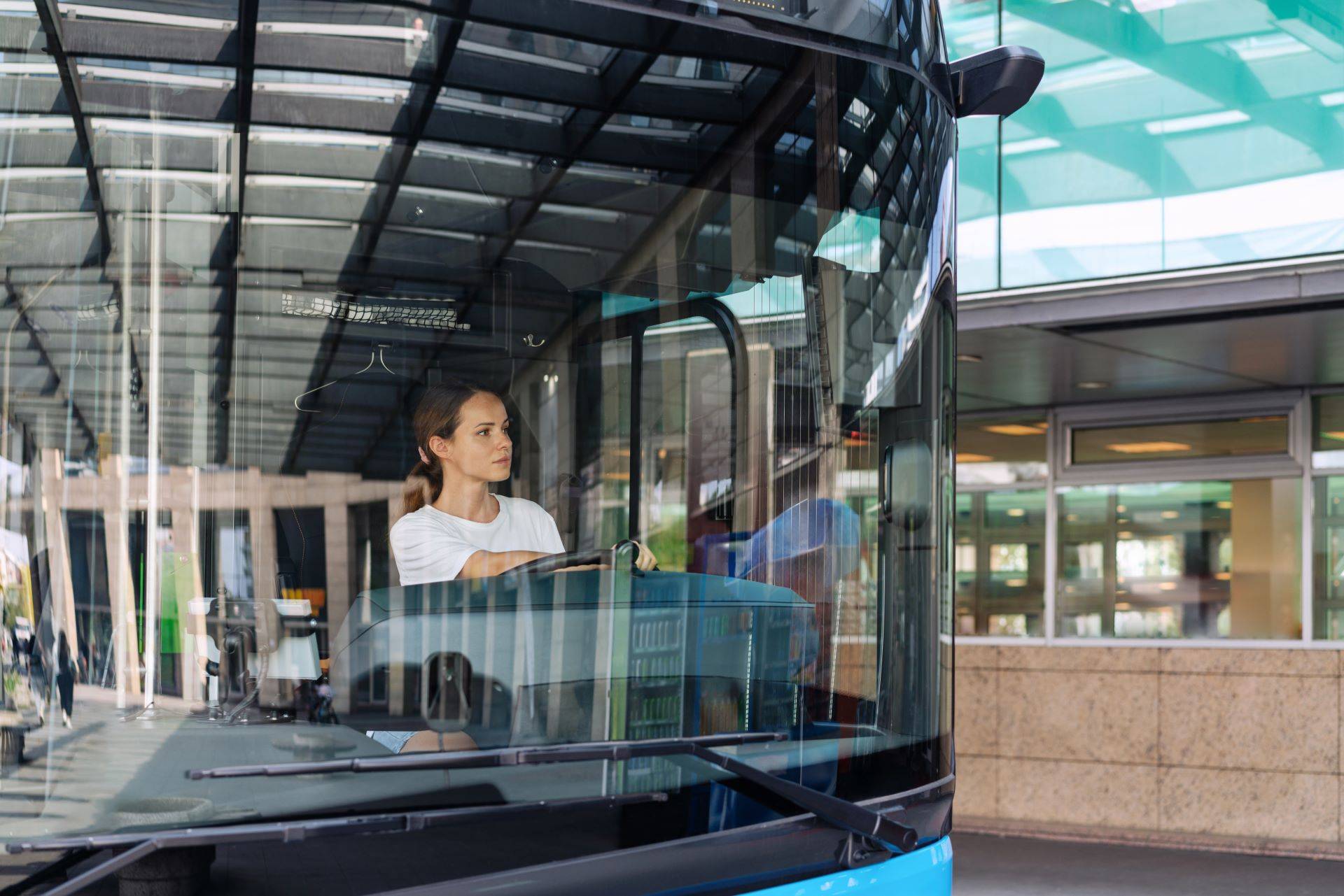 Busfahrerin fährt modernen Linienbus an Haltestelle