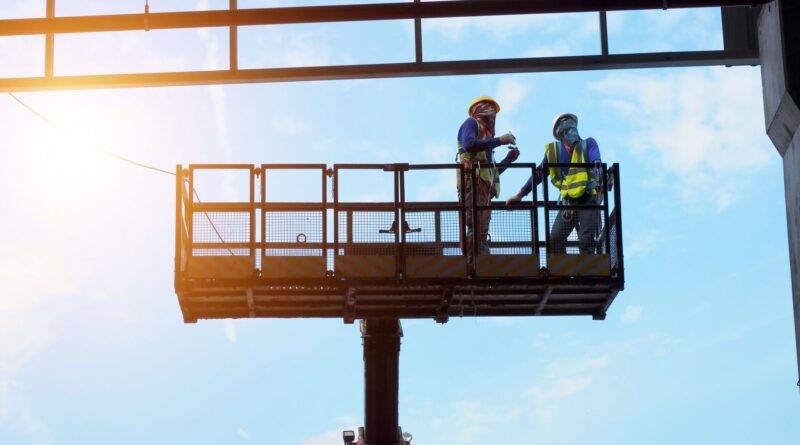 Zwei Bauarbeiter auf Arbeitsbühne im Stahlbau unter blauem Himmel in Oberhausen
